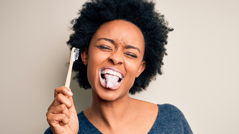 Woman brushing her teeth and tongue with toothbrush and toothpaste