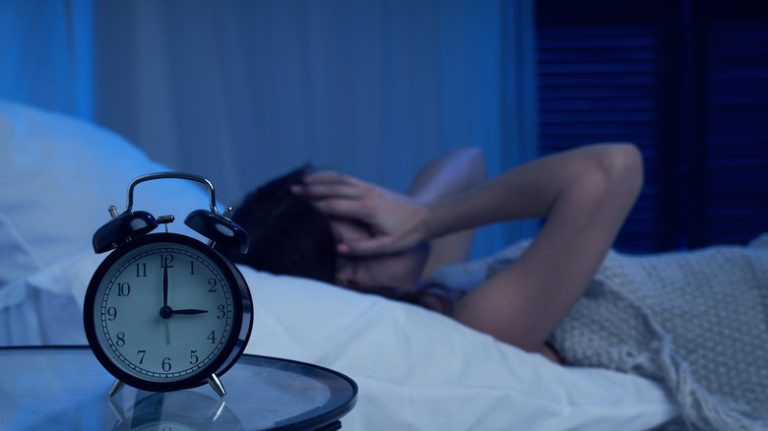 woman laying stressed out in bed with alarm