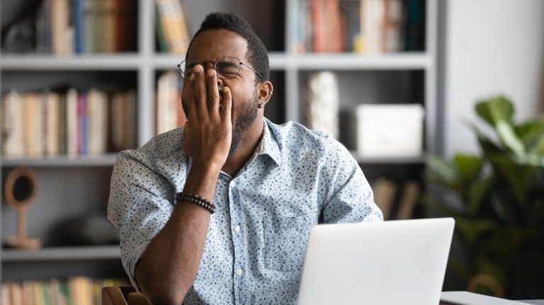 A man yawning at his computer during the day