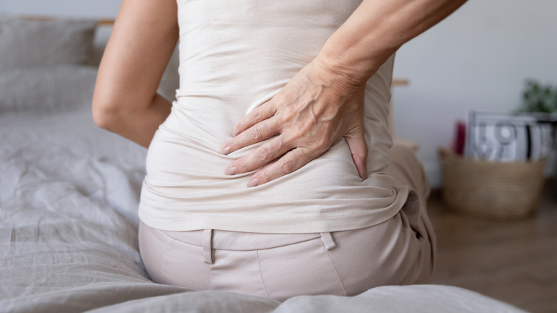 woman sitting on bed holding lower back