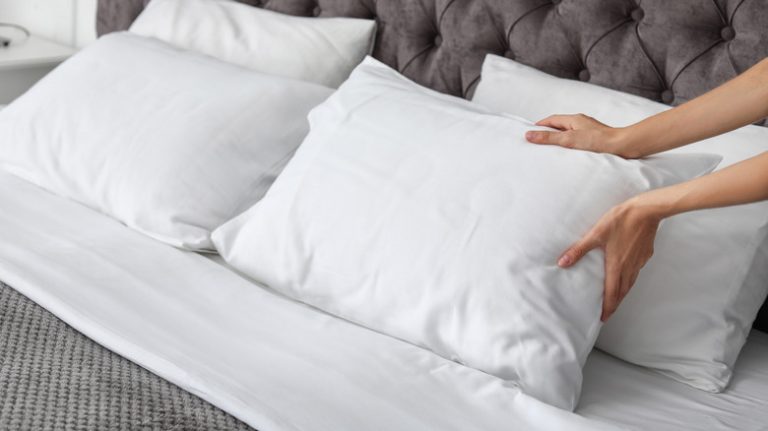 Person prepping pillows on bed