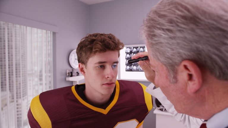 Doctor using flashlight to look at the pupils of a football player