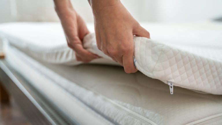 Close up of hands holding a mattress topper atop their mattress