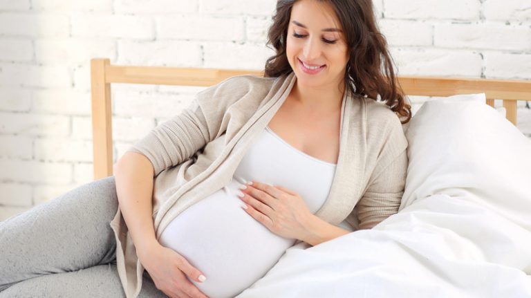 pregnant woman holding belly in bed
