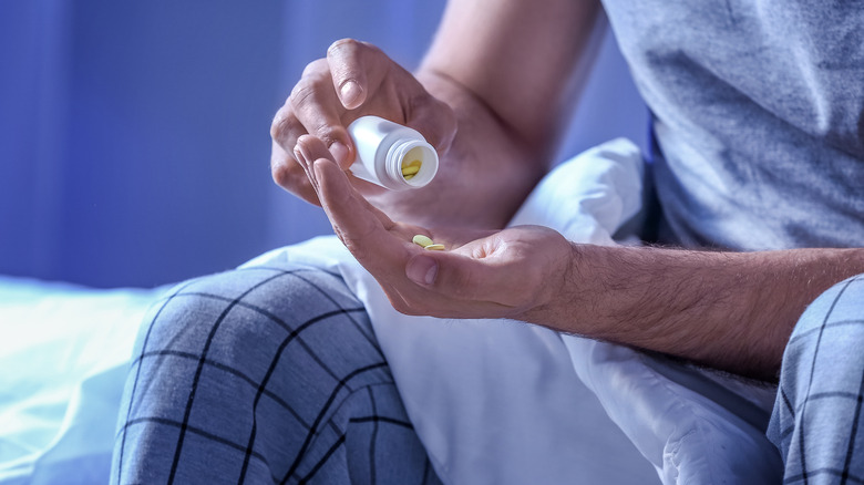 young man sitting on bed taking sleeping pill