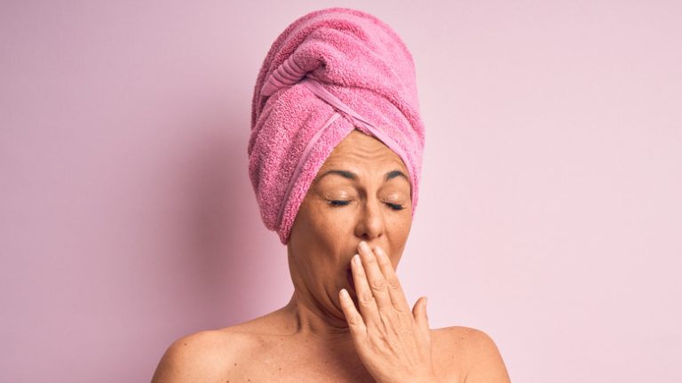 woman in a pink towel yawning with isolated pink background