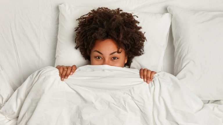 Woman smiling and laying under a blanket