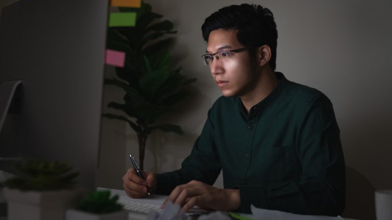 A man working at his computer in a darkened room