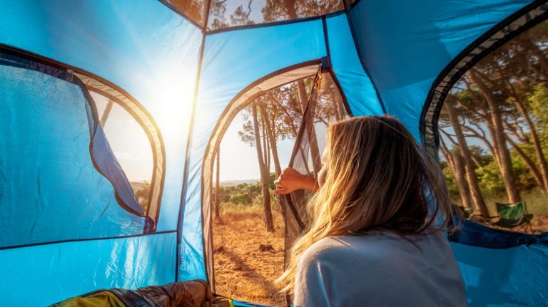 woman waking up in a tent in the woods