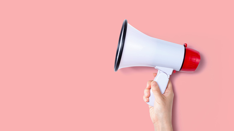 a hand holding a megaphone over a pink background