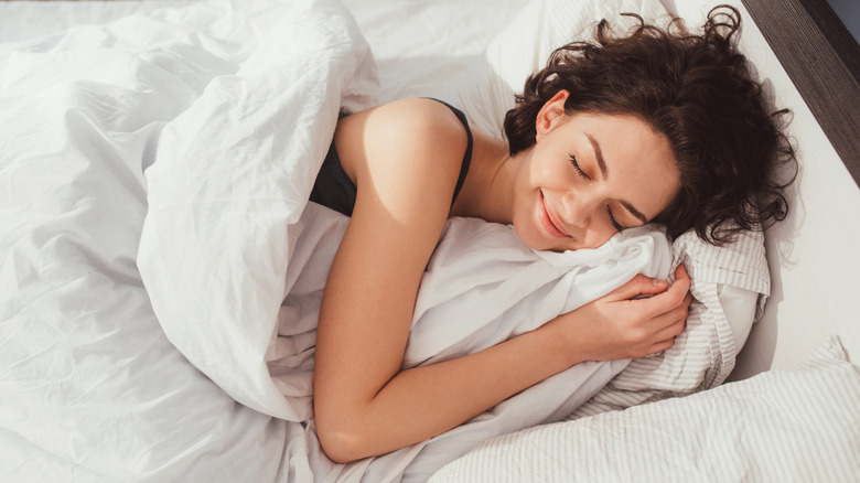 Woman lying in bed and with eyes closed while covered with blanket