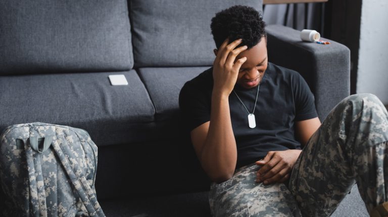 Soldier sitting in front of a couch with his hand on his head