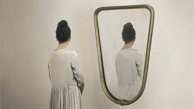 woman looking in mirror with reflection facing away from her