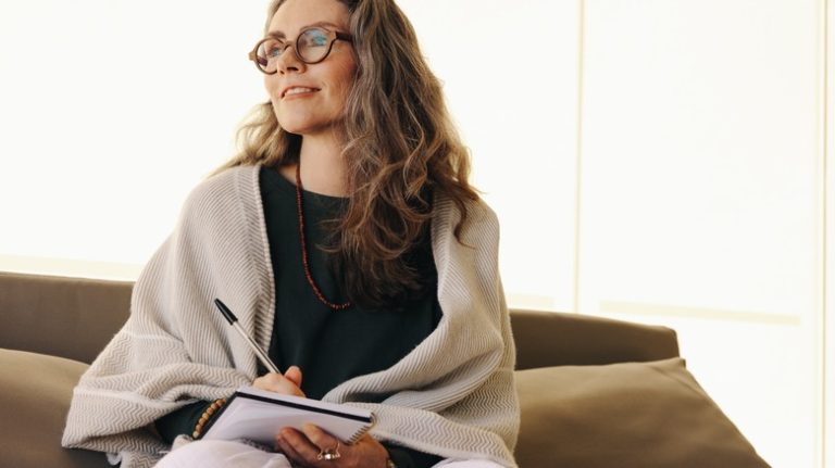 woman smiling and reflecting while writing in a journal