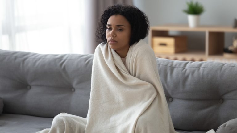 An anxious woman sitting on her couch wrapped in a blanket