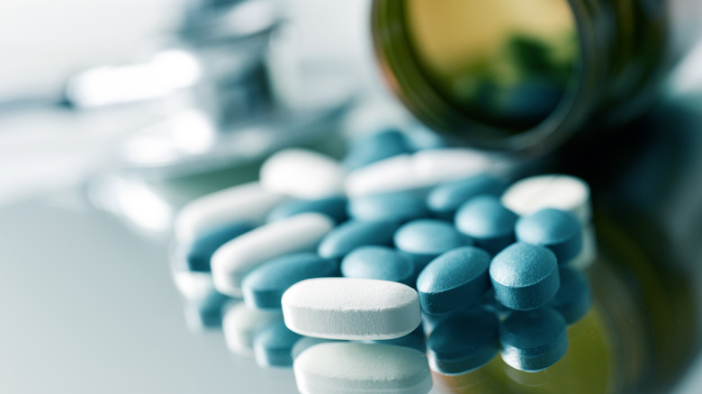 close up of two prescription pills and a bottle tipped over