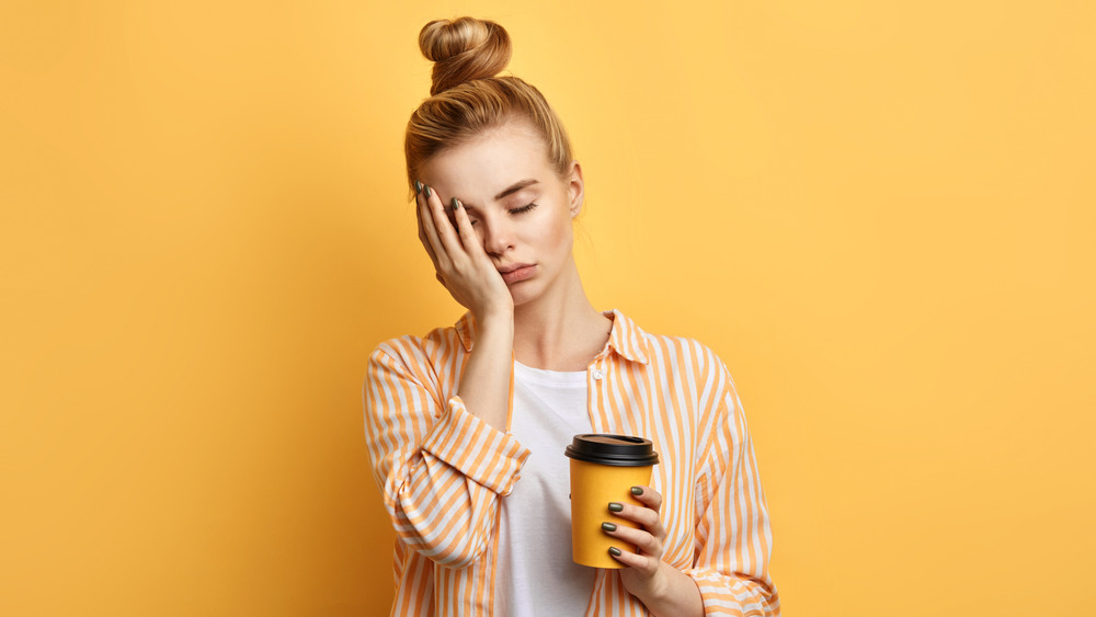 Woman hold cup of coffee with eyes closed and hand on face