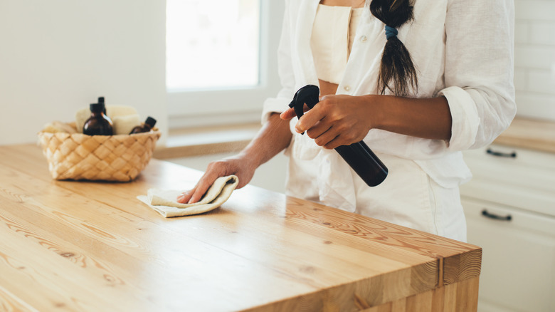 woman using spray and rag to clean wood furniture